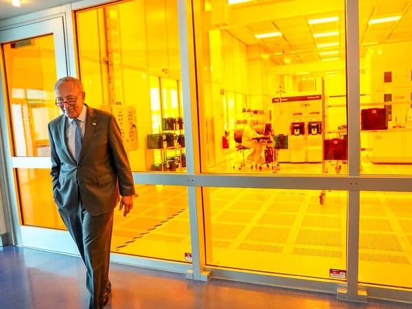 Senator Chuck Schumer walking away from an illuminated building with large glass doors.