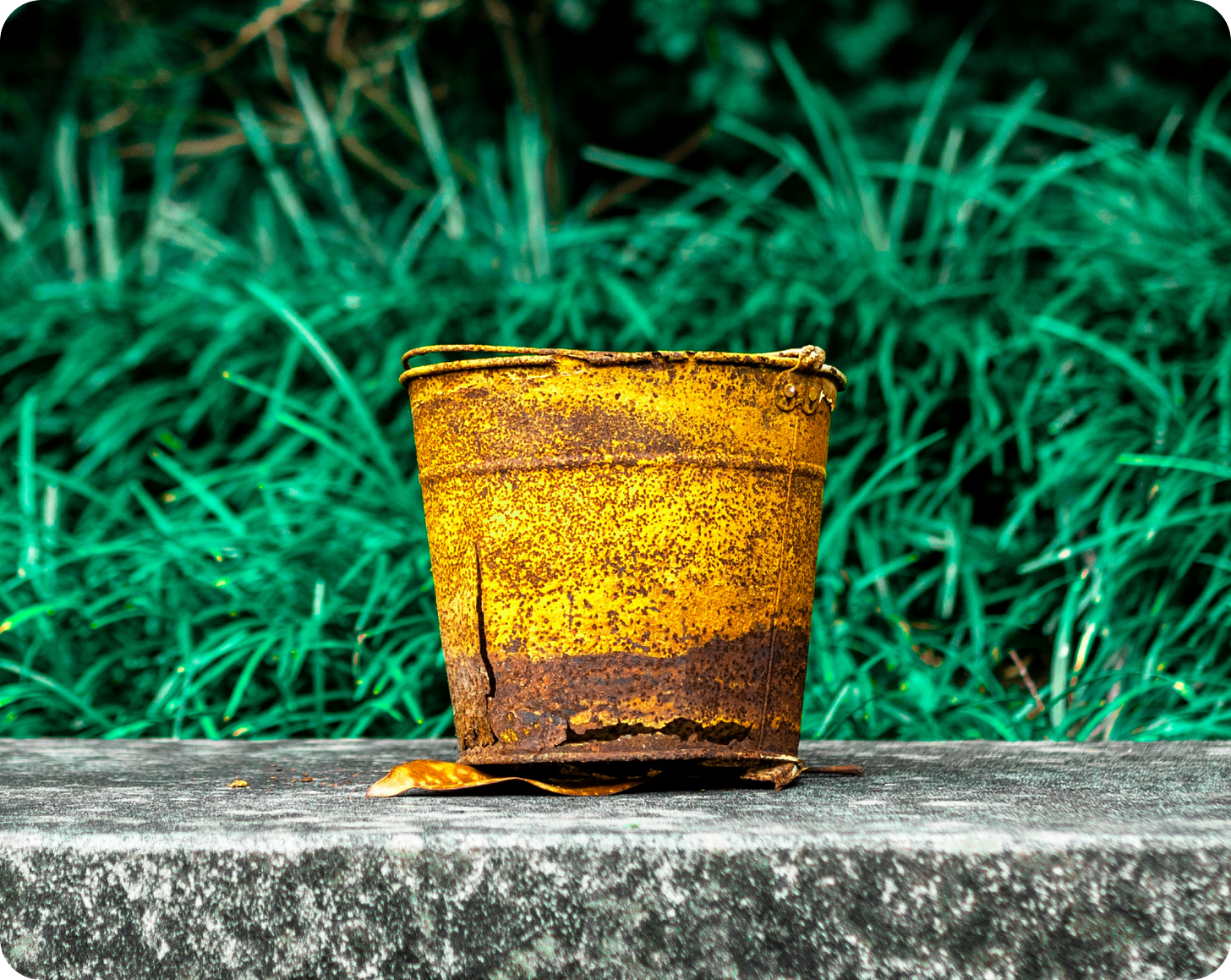 Photograph of a old rusty metal bucket with a hole in the bottom.