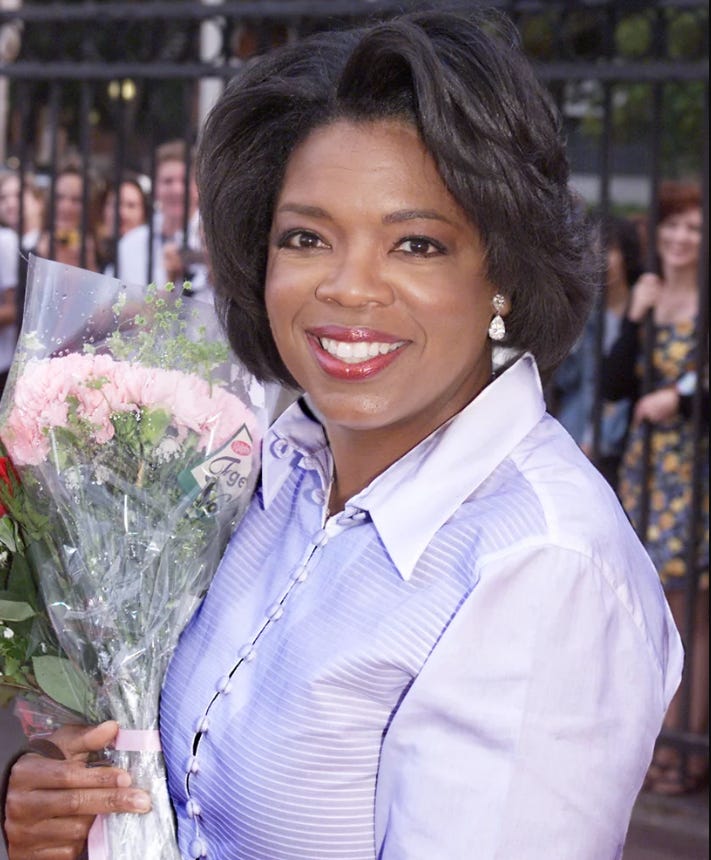 Image of Oprah Winfrey, the true start of her universe, holding flowers while surrounded by adoring fans.