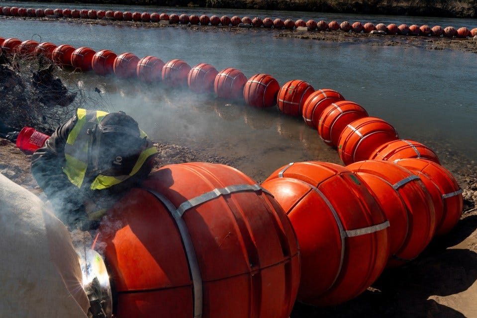 A worker welds together a line of orange buoys in a river.