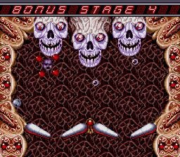 A screenshot of Bonus Stage 4 from Devil's Crush, featuring three grinning, bloodshot-eyed skulls at the top of the screen, with two sets of flippers at the bottom. Floating heads with red balls surrounding them block the path to the skulls above.