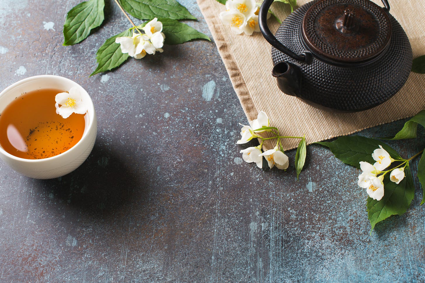 Jasmine tea teacup with teapot, leaves and flowers on dark texture, top view of the table