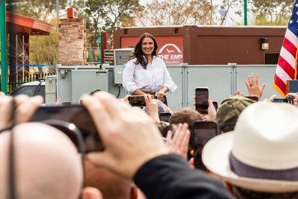 A picture of Representative Alexandria Ocasio-Cortez of New York smiling as she appears at an event in North Las Vegas, Nev. In the foreground are people holding up phones for pictures or video. 