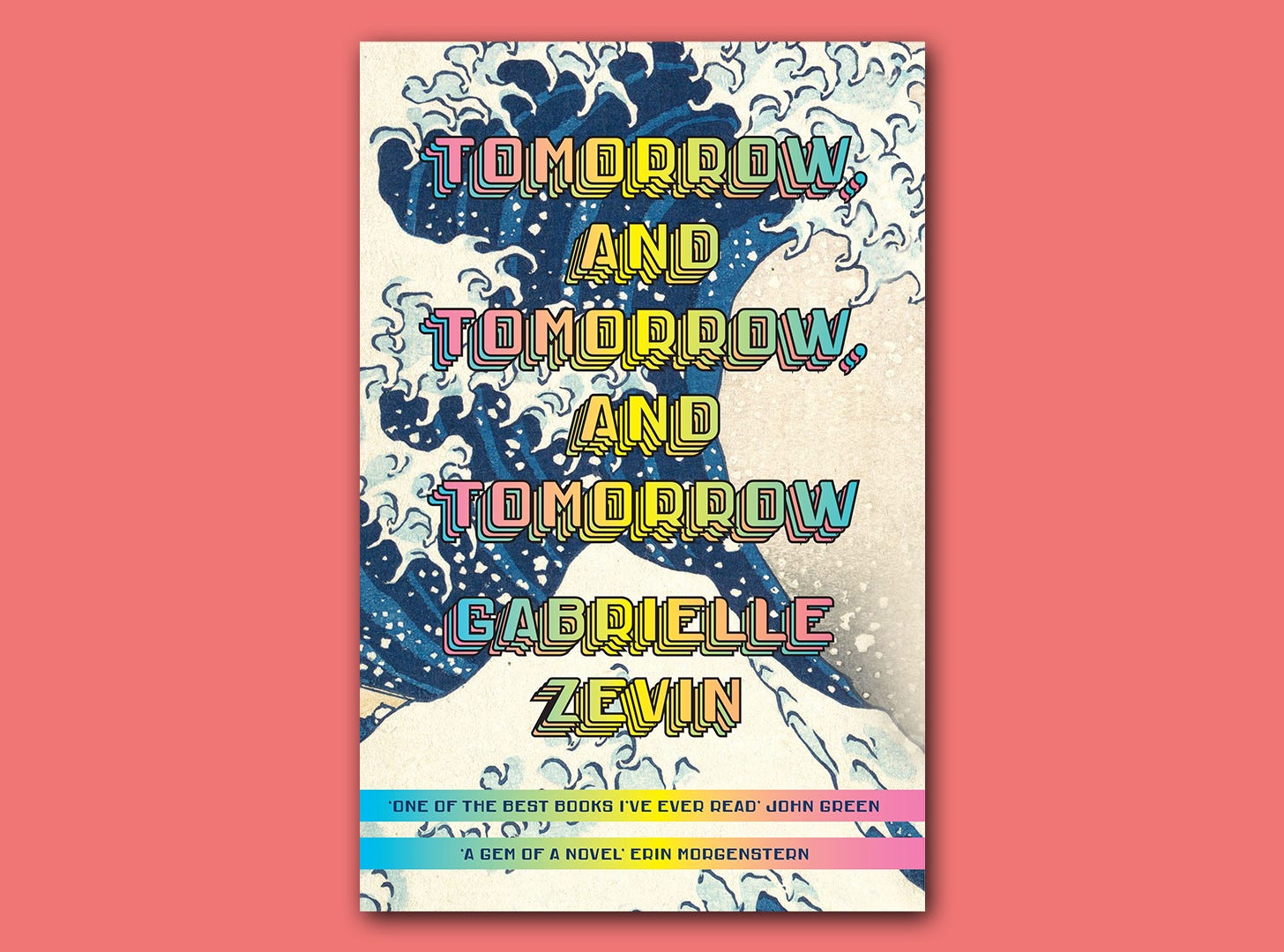 The book cover for "Tomorrow, and Tomorrow, and Tomorrow" by Gabrielle Zevin superimposed on a light pink block colour background. The book cover is a close up of "The Great Wave of Kanagawa" which is a famous woodblock print by the Japanese artist Hokusai. It is a giant wave swelling and ready to crash onto shore. The title is printed over this image in big, bold, rainbow, capital letters.