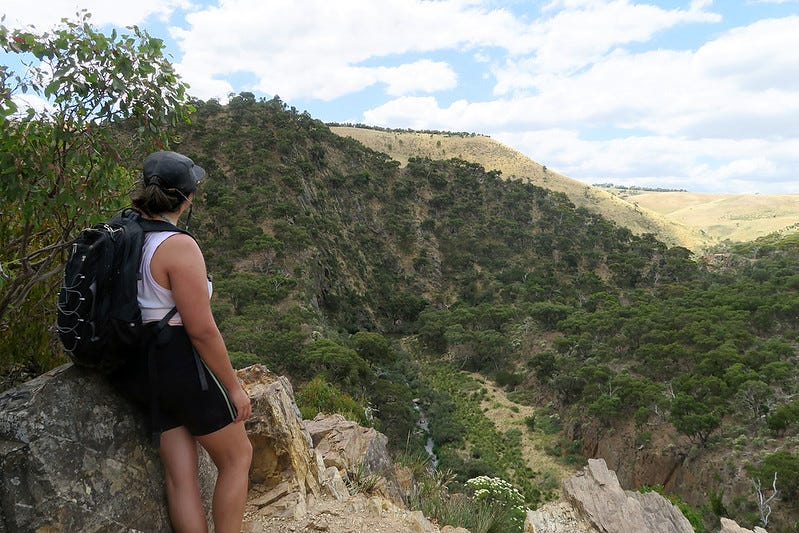 A woman in hiking gear stands looking out at hills.