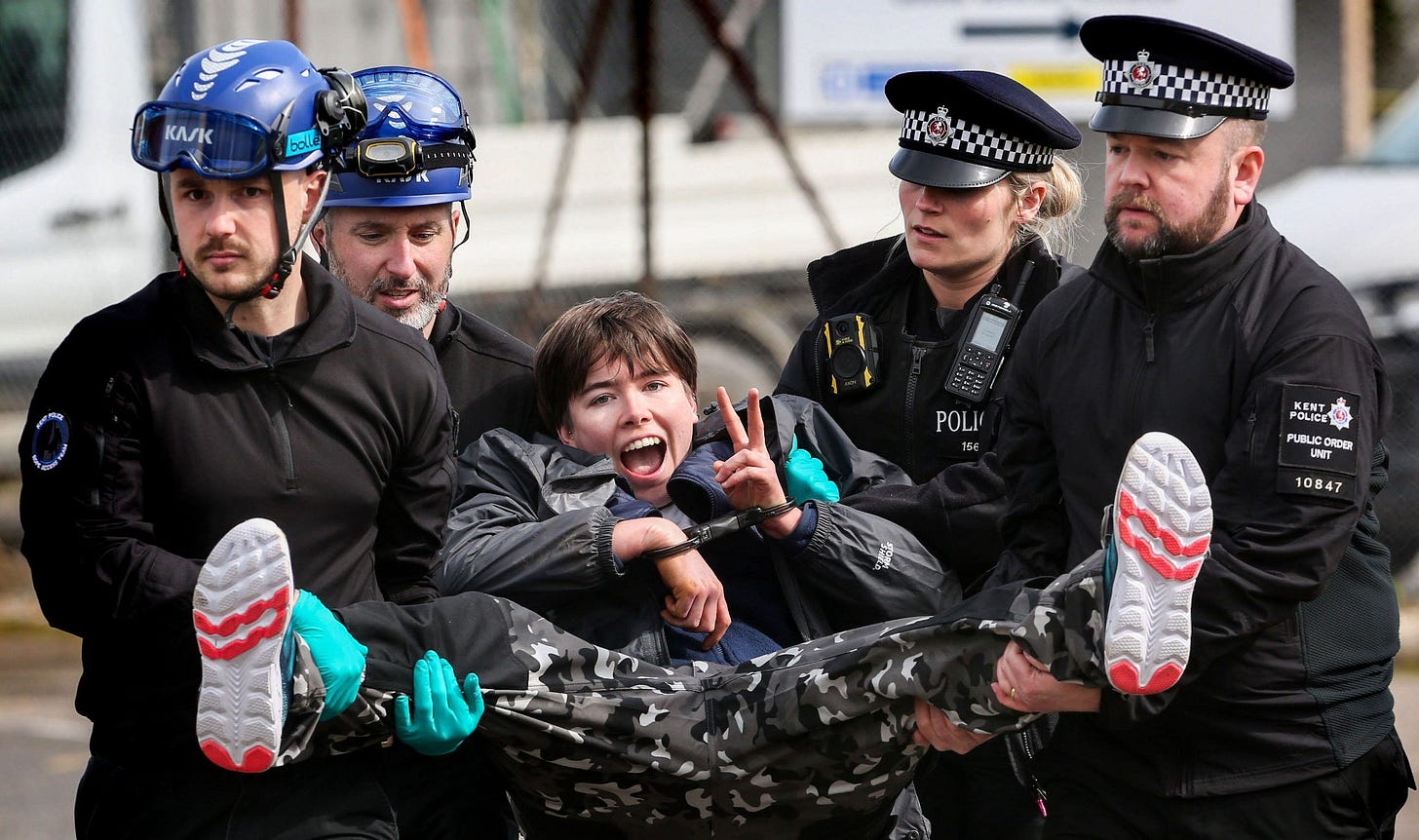 An activist is handcuffed and carried by four enforcement officers after refusing to walk following her arrest outside Instro Precision during the demonstration. Instro Precision provide components for Elbit Systemis weaponry. Palestine Action continues to target subsidiary companies of Israeli arms company Elbit Systems in an attempt to isolate them and make business impossible. This tactic has caused two of Elbit's ten main businesses to close in the UK and several partner companies to cut ties with them.