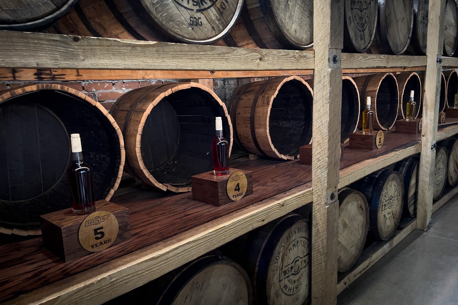 Whiskey barrels and bottles in front of each demonstrate how the color changes during the aging process