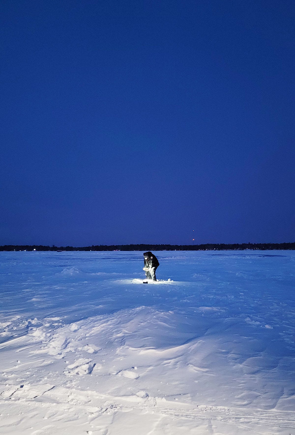 Drilling a hole in the ice at night. 