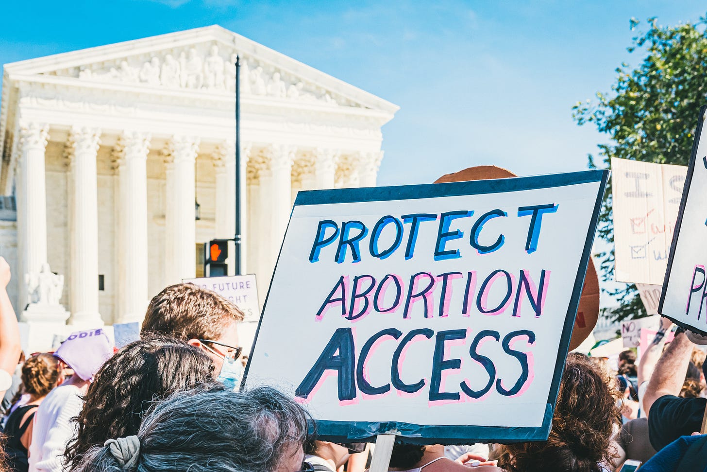 A close-up of a handwritten sign at an abortion rights protest. The sign says ‘PROTECT ABORTION ACCESS.’ Photo by Gayatri Malhotra on Unsplash