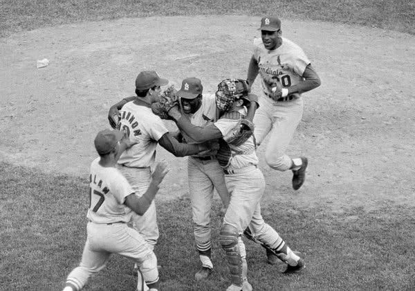 A black-and-white image on four baseball players, including a catcher, rushing to embrace the pitcher Bob Gibson at the conclusion of a World Series game in 1967.