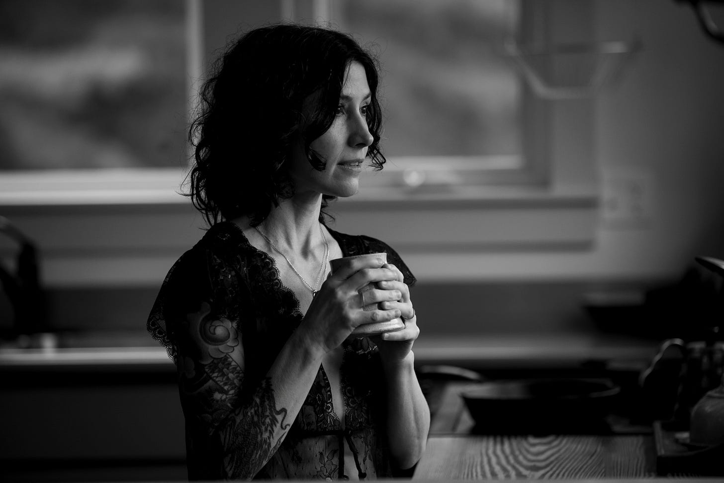 Author standing in kitchen holding a coffee mug, looking pensive, in black and white