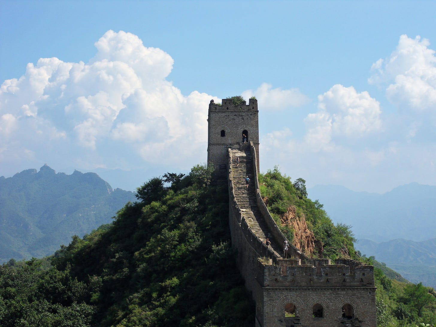 The Great Wall of China extending up a steep hill under a blue sky with big billowing white clouds