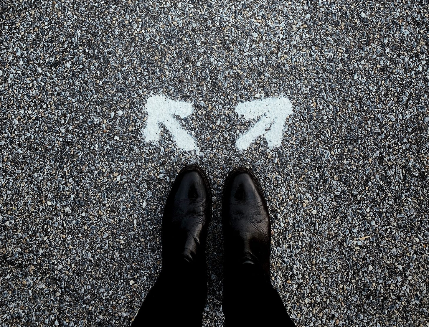 A person's feet in black shoes standing on a path ready to choose a direction.