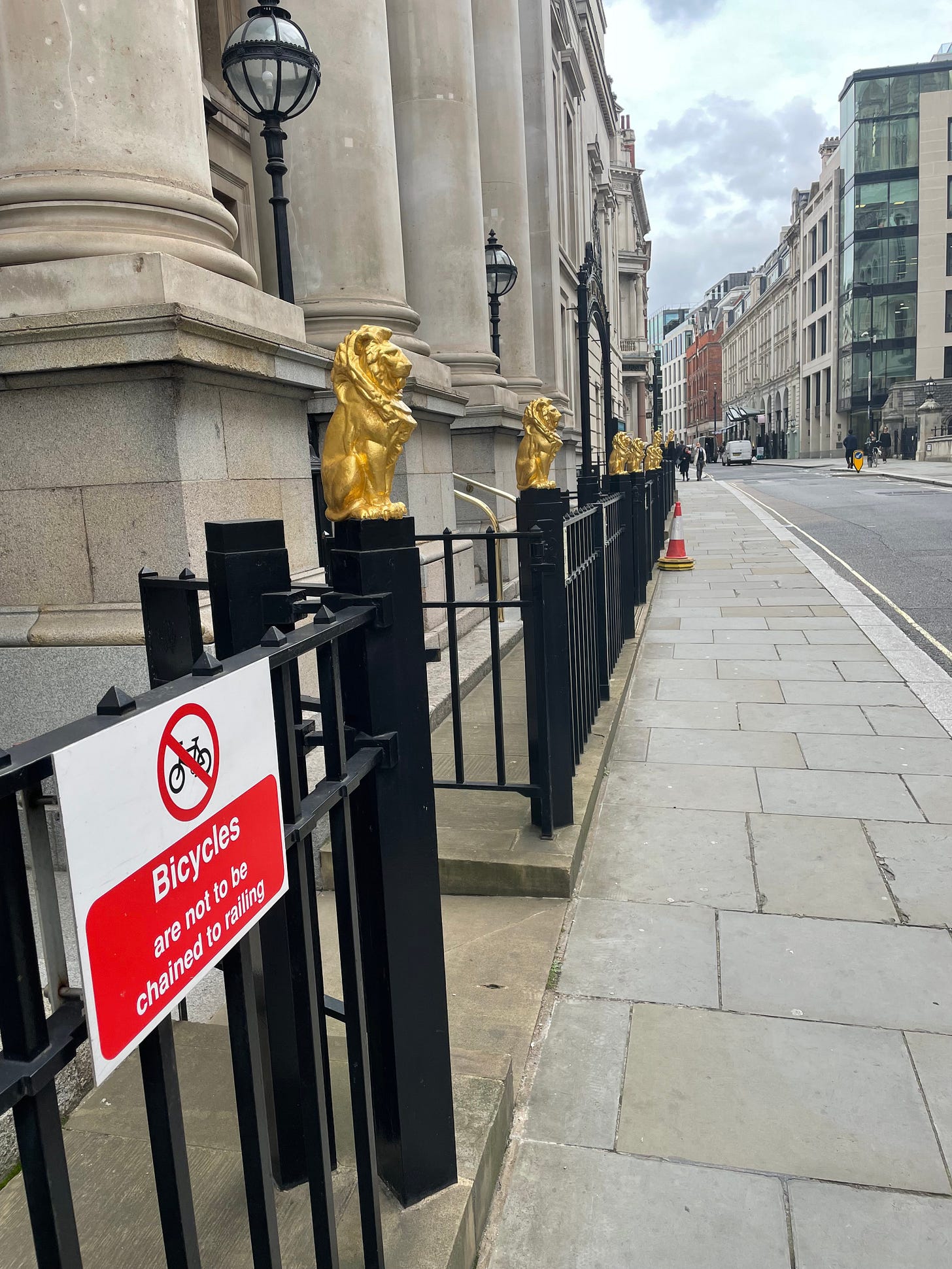 Golden lions on black railings, along a pillared building on a London street