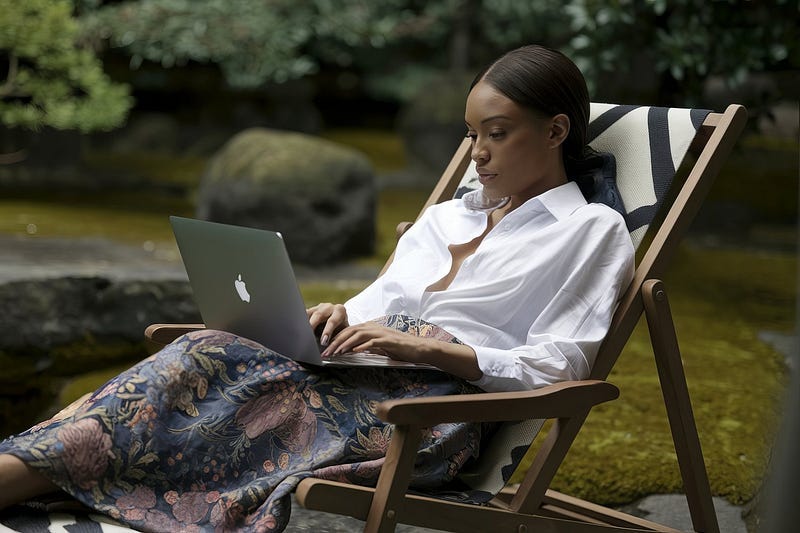 African woman sitting on a deck chair in a Japanese garden typing on her MacBook Pro.