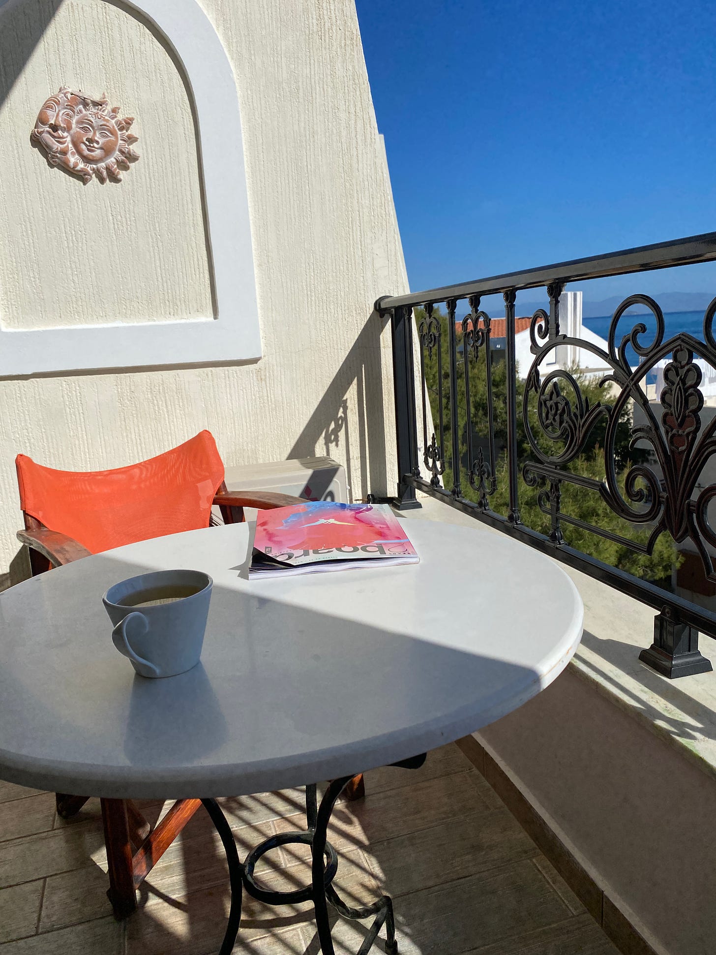 A bright blue sky. A balcony with a table, a cup of coffee and a two suns joined and smiling together on the wall behind.