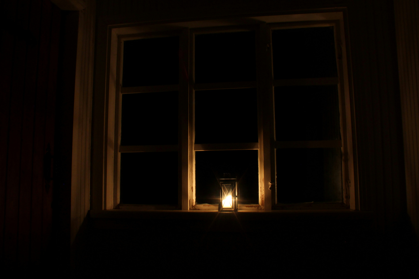Photograph of a dark room with a lamp on the windowsill. The lamp gives off a warm golden glow.