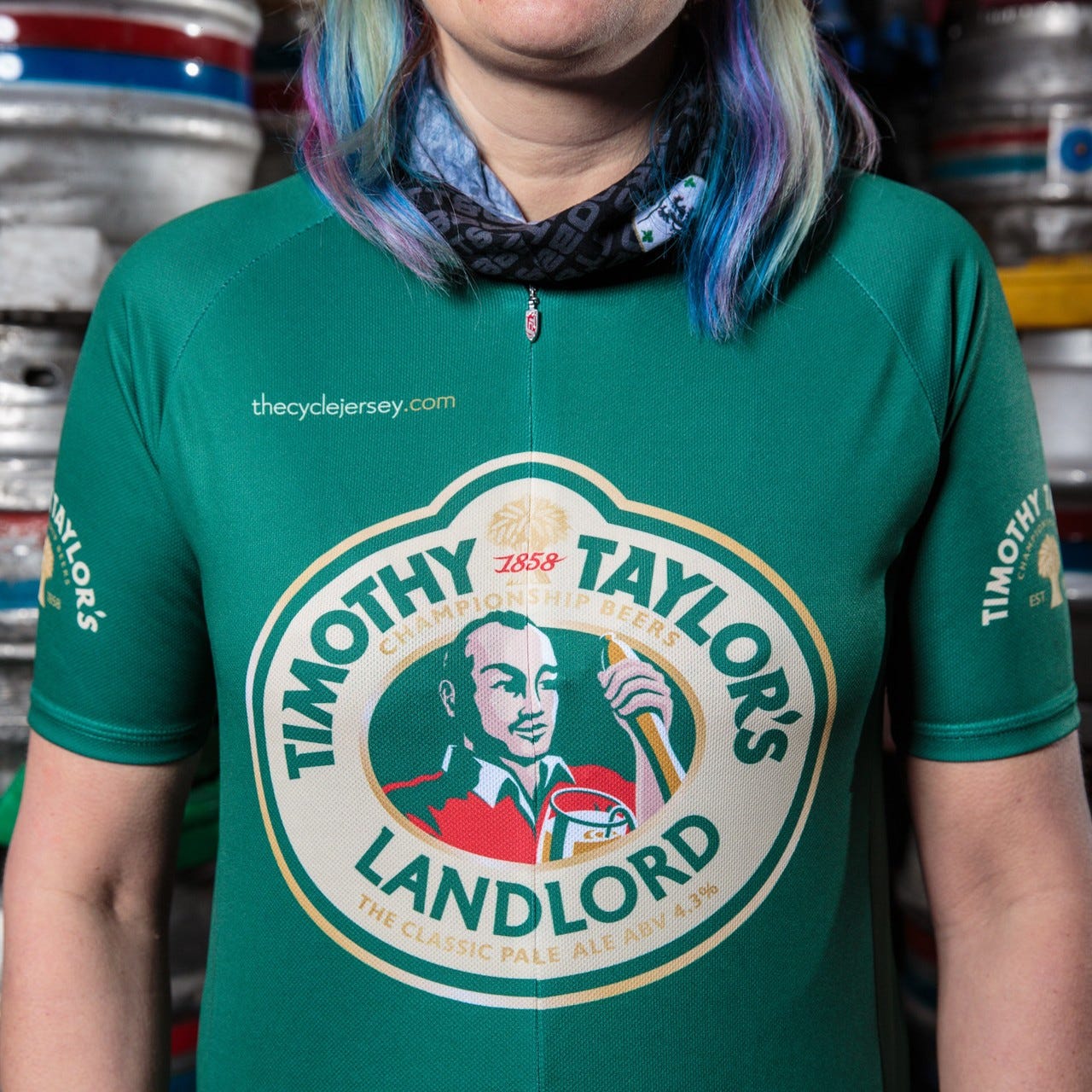 Model with purple, green and blue hair wears a green cycling jersey with a large Timothy Taylor's Landlord logo on the front, and small gold versions on each sleeve. It's a short sleeved jersey.