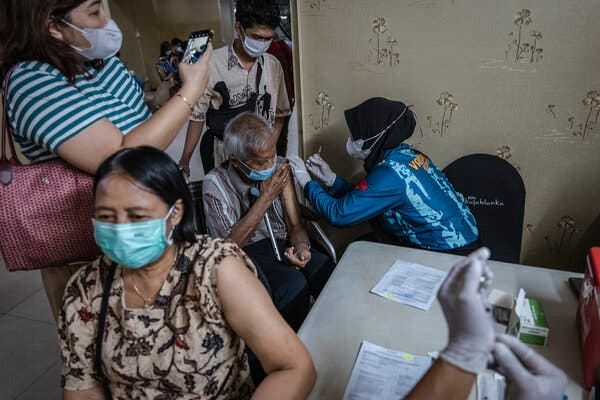 A man and a woman receive a booster vaccine from medical workers as two people stand nearby.
