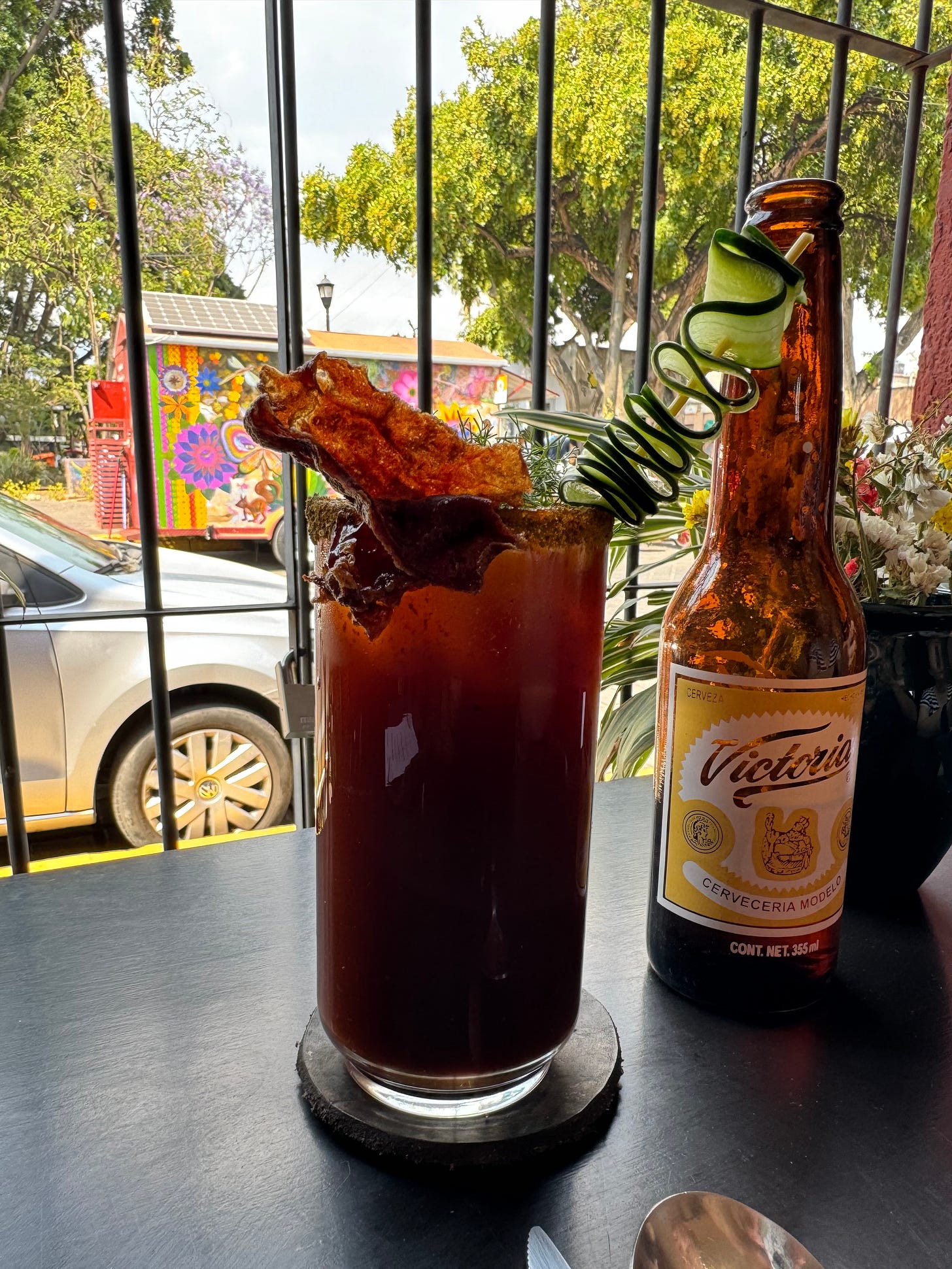 A tall glass filled with clamato, with a garnish of cucumber and bacon.