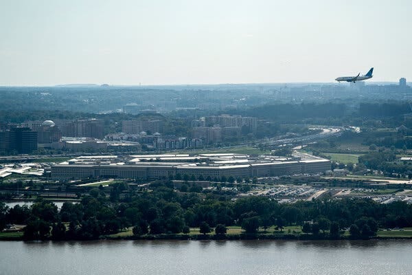 A plane flying over the Pentagon with trees and water in the foreground. 