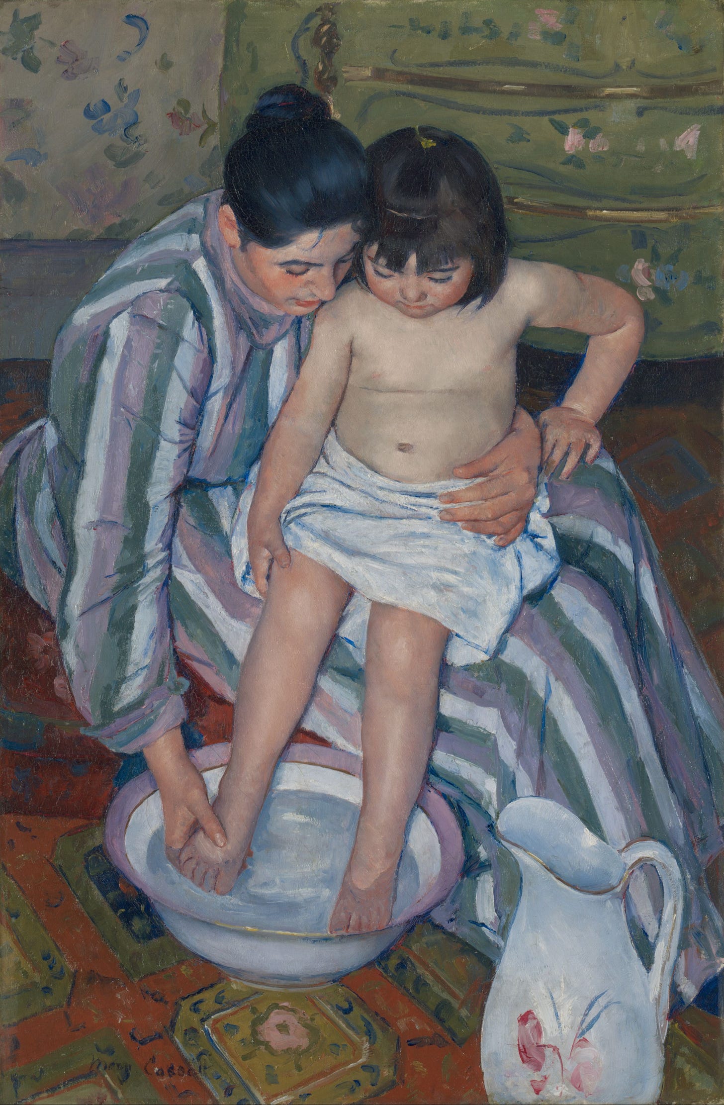 The woman is sitting on an oriental carpet, with the child on her knees. The child has a white cloth swathed around their abdomen, and the woman is wearing a dress with strong vertical stripes of green, pink and white. The woman holds the infant firmly and protectively around its waist with her left hand while the other hand carefully washes the child's bare limbs in a basin of water, resting on the floor beside a jug decorated with a floral pattern. The chubby left arm of the child braces against the mother's leg, while their other hand grips the child's own right thigh. The mother's right hand presses firmly but still gently on the child's right foot in the basin, mimicking the child's own pressure on her thigh. In the background are floral patterns of painted furniture and wallpaper. The woman is sitting on an oriental carpet, with the child on her knees. The child has a white cloth swathed around their abdomen, and the woman is wearing a dress with strong vertical stripes of green, pink and white. The woman holds the infant firmly and protectively around its waist with her left hand while the other hand carefully washes the child's bare limbs in a basin of water, resting on the floor beside a jug decorated with a floral pattern. The chubby left arm of the child braces against the mother's leg, while their other hand grips the child's own right thigh. The mother's right hand presses firmly but still gently on the child's right foot in the basin, mimicking the child's own pressure on her thigh. In the background are floral patterns of painted furniture and wallpaper.