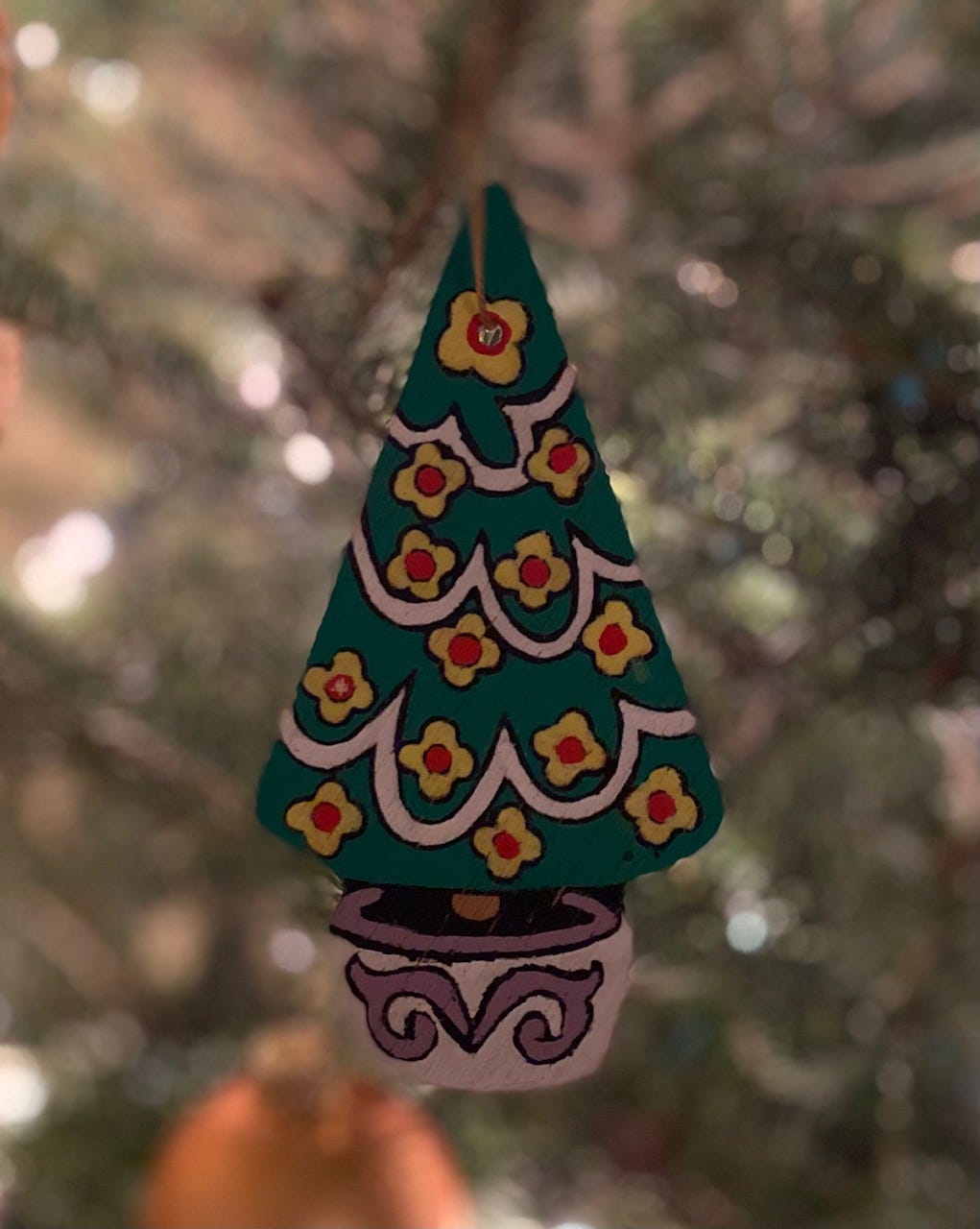 Wooden ornament hanging on tree, painted green with white swoops of garland and yellow flowers with red centers. From 1970s,