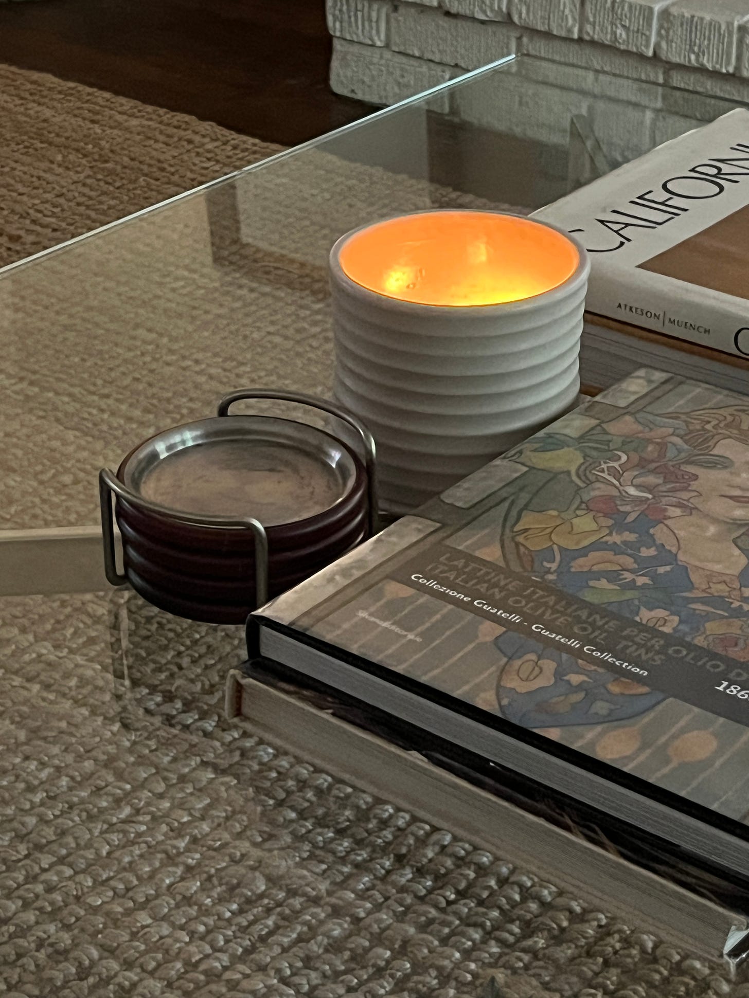 A lit candle sitting atop a coffee table nestled between coasters and books.
