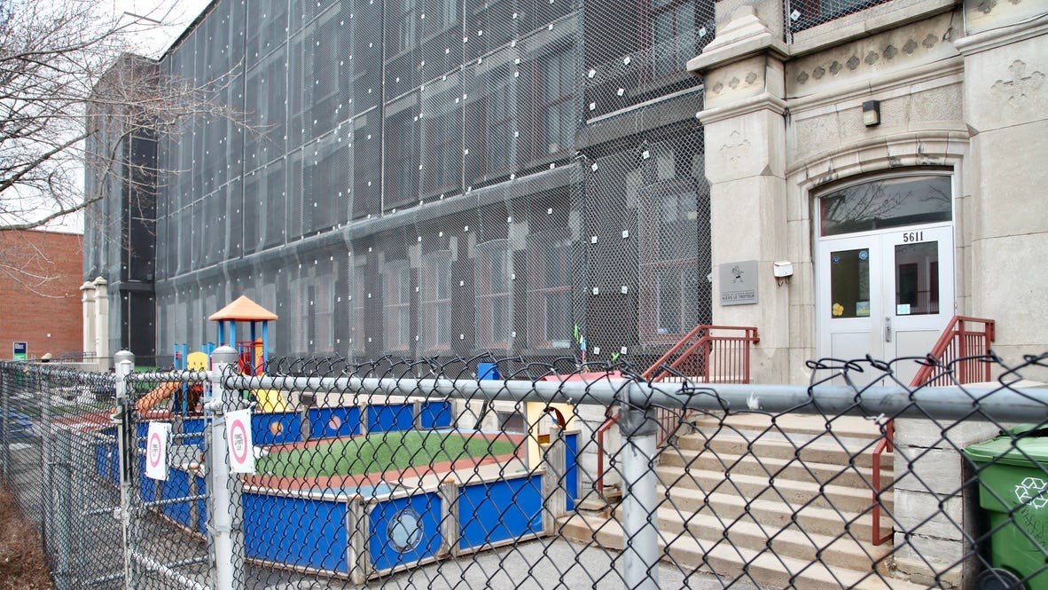 On voit la façade ouest du bâtiment, le long de la rue Clark, qui est recouverte de grilles de protection, ainsi que l’entrée principale et la cour du CPE Alexis le Trotteur.