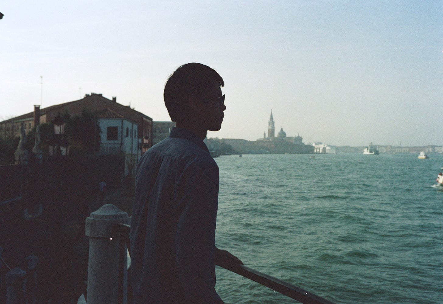 An Asian man looks over the canals of Venice as ships go by.
