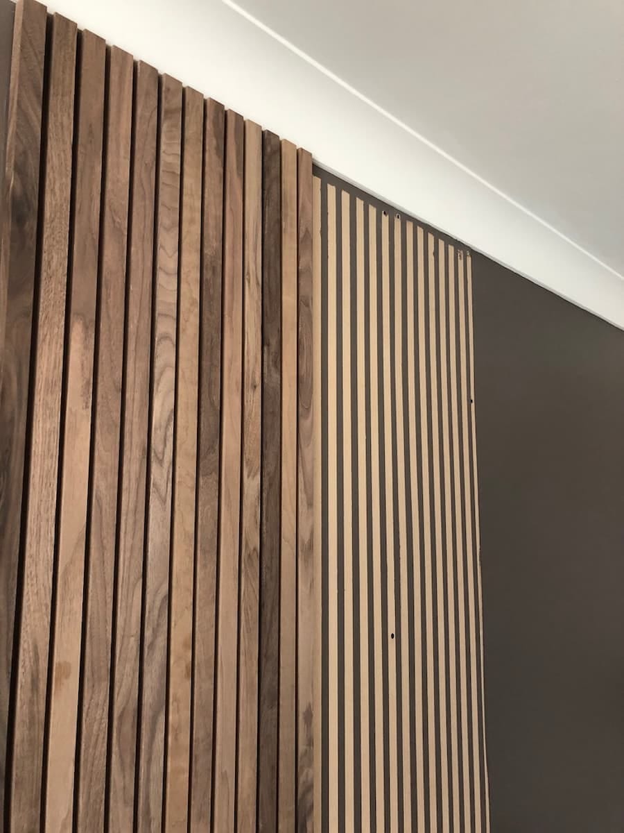 MDF board attached to the wall which has been painted with brown vertical stripes, which are used as markets to position the wooden batons onto for creating the wooden feature wall.