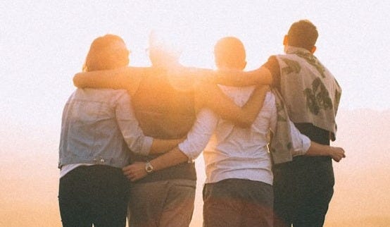 four person hands wrap around shoulders while looking at sunset four person hands wrap around shoulders while looking at sunset