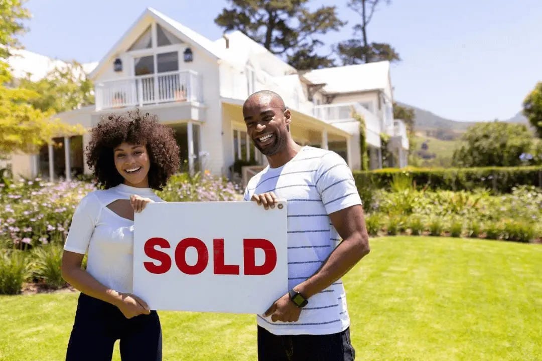 Couple holding sold sign in front of their recently sold home