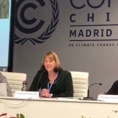 Middle aged blonde woman sits at conference seat in front of UN conference sign