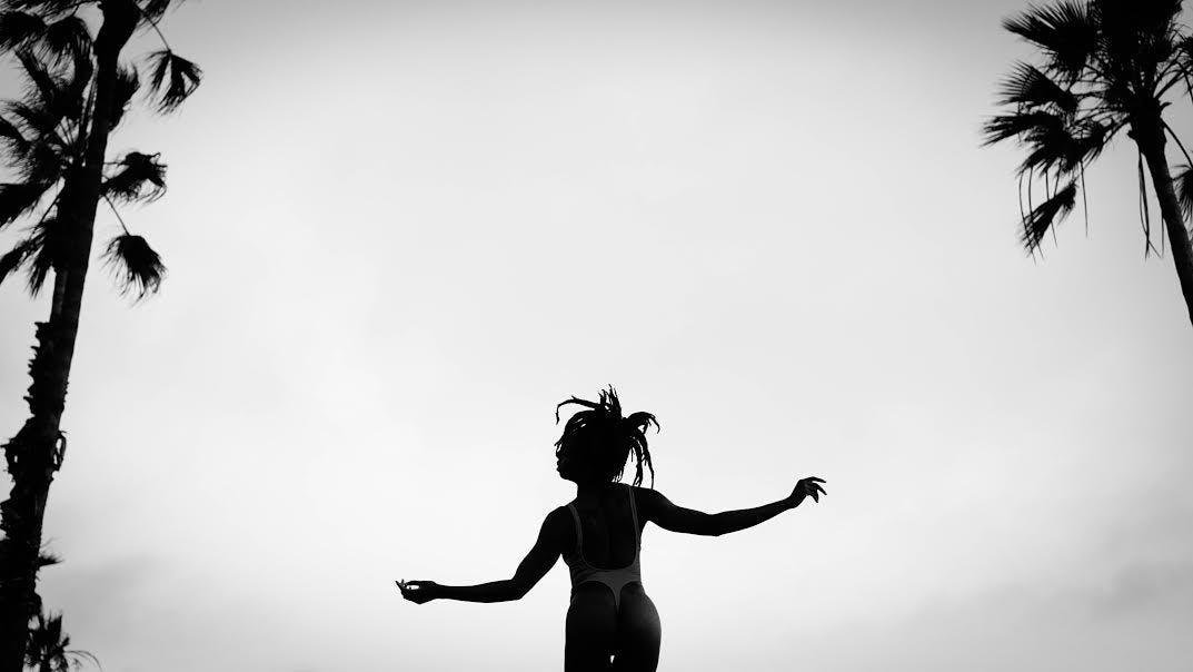 black and white image of n3vlynnn dancing gracefully at the beach between two palm trees