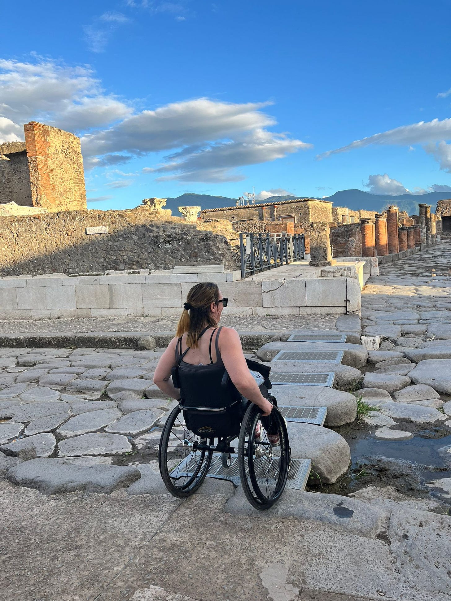 A clear day in Pompeii: in my wheelchair, I cross over the access routes placed on the old Roman roads in Pompeii, which are just large lumps of rock lined up like gigantic cobblestones. 