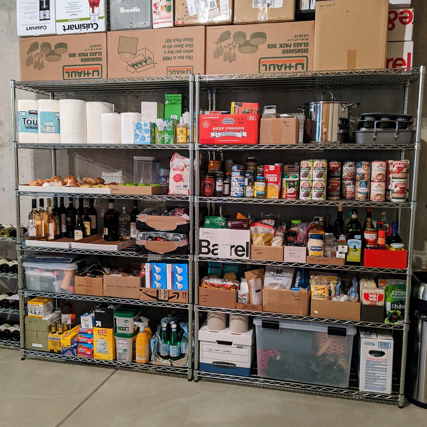 Two tall shelving units with cans of beans, tuna, tomatoes, bottles of wine, etc.