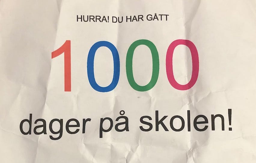 Crumpled sheet of white paper with the words "Hooray you have been at school for 1000 days" printed in Norwegian, the number 1000 in different colours.