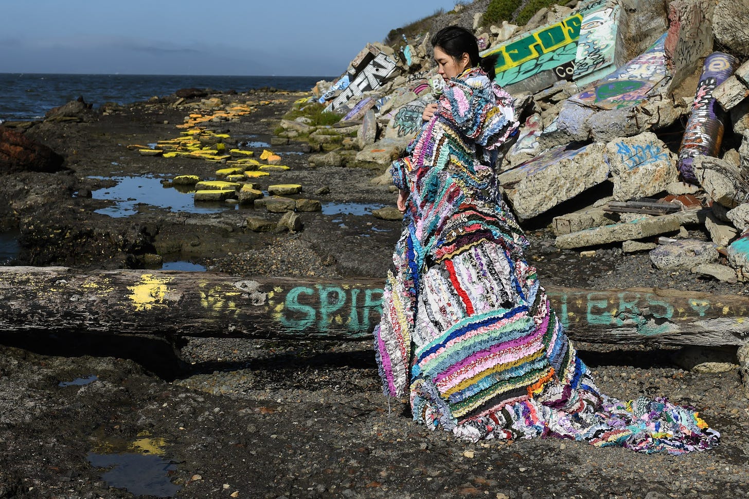 Woman wearing a dress made of recycled gathered cloths by Mira Musank standing on a rocky shore