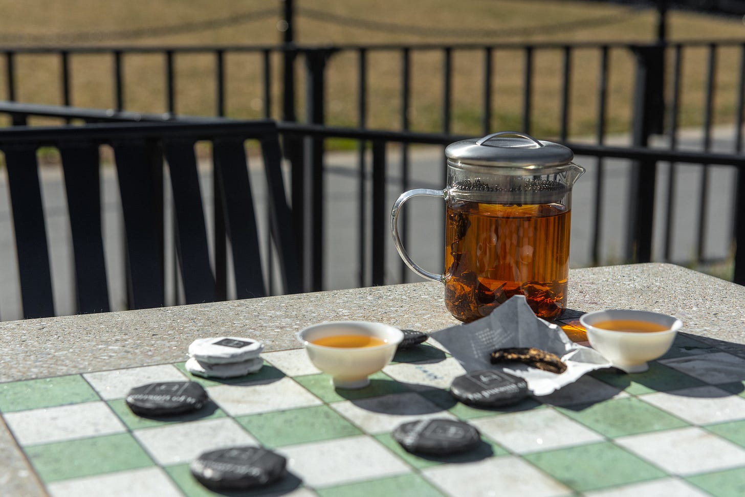 ID: Tea cakes, pot of tea, and cup on a concrete chess table at a park