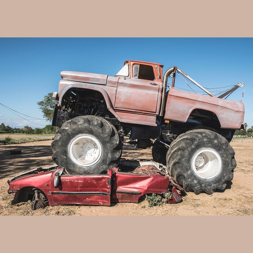 A monster truck on an crushign a car beneath its humongous tires.