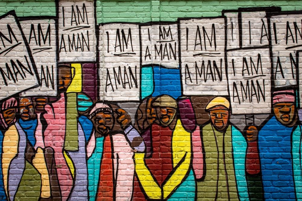 Photo of a mural of POC men holding up signs that read, "I am a man."