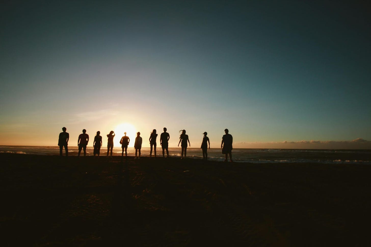 11 people, silhouetted before a sun low on the horizon.