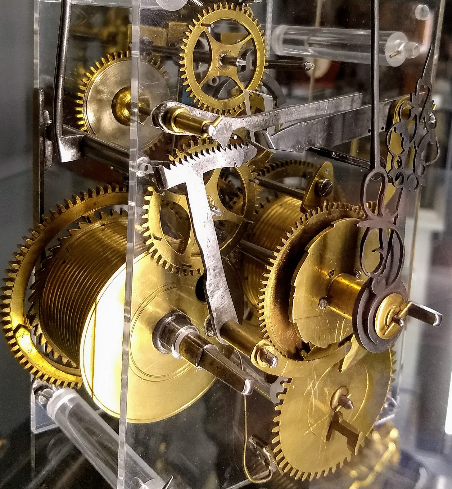 A clear perspex case encloses a complex clockwork arrangement of brass cogs, balance levers, springs and wheels.