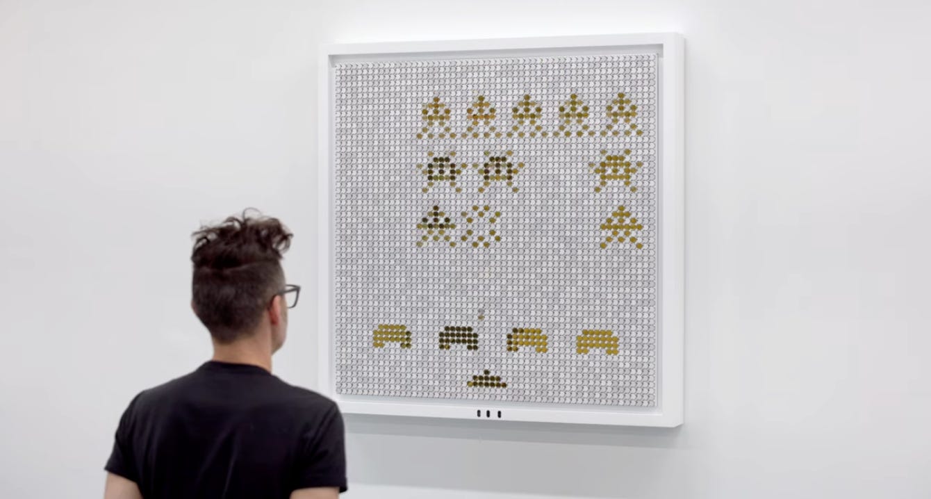 A man in a black t-shirt stands in front of an interactive artwork showing the arcade game Space Invaders