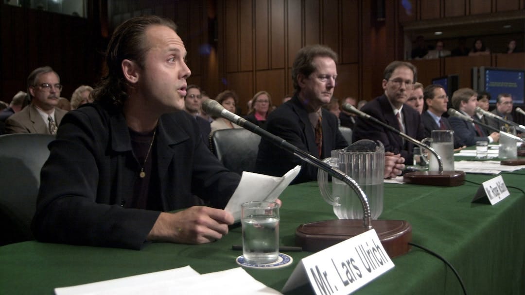 A photo of the Metallica drummer, Lars Ulrich, reading his statement to Senate behind a table covered in green cloth A photo of the Metallica drummer, Lars Ulrich, reading his statement to Senate behind a table covered in green cloth