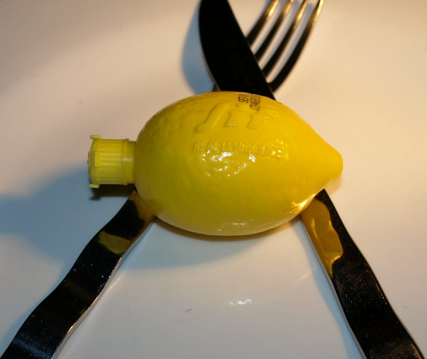 A plastic lemon sitting on a plate on top of silverware