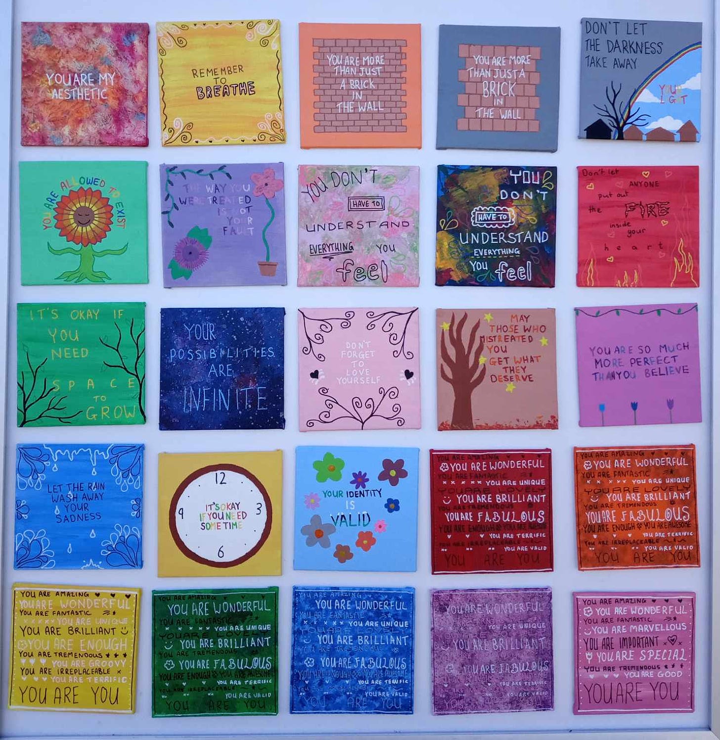 photo of 25 small paintings in a 5x5 setup. they each have a positive quote and some little doodles. some are more detailed than others.