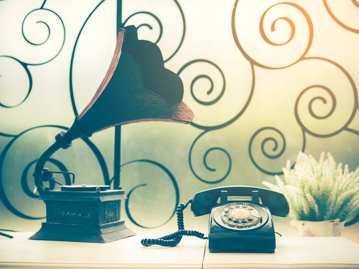 Close-up of a black rotary phone and an ornate gramophone on a table.