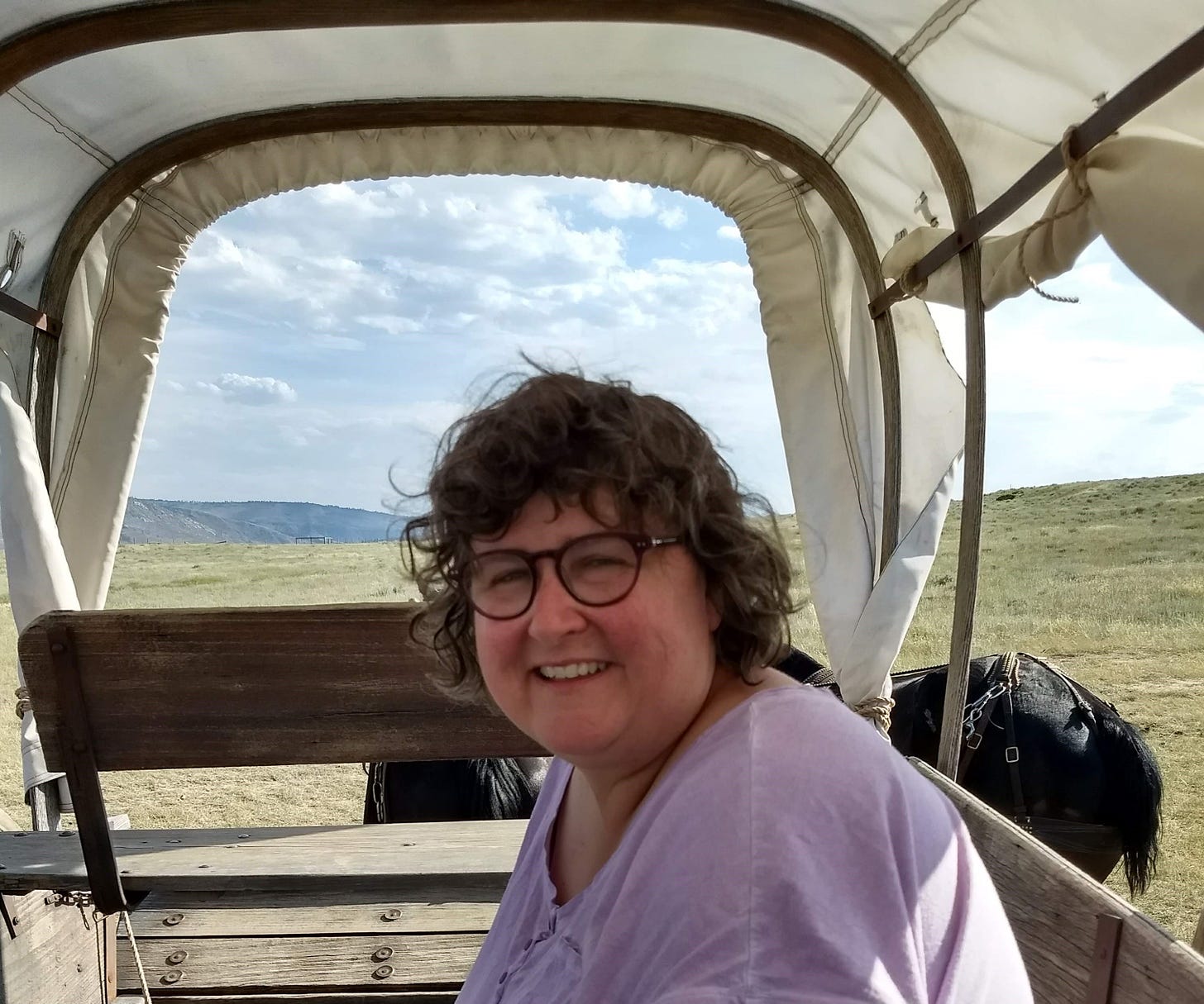 Annette sitting in covered wagon with two horses in Wyoming